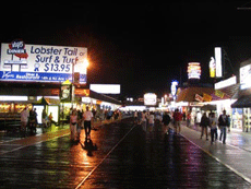 People on a boardwalk at night, with shops to the left.